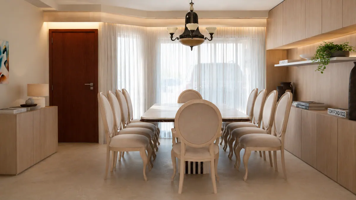 Sala de jantar com mesa longa, lustre, cortinas de linho e porta de madeira escura ao fundo