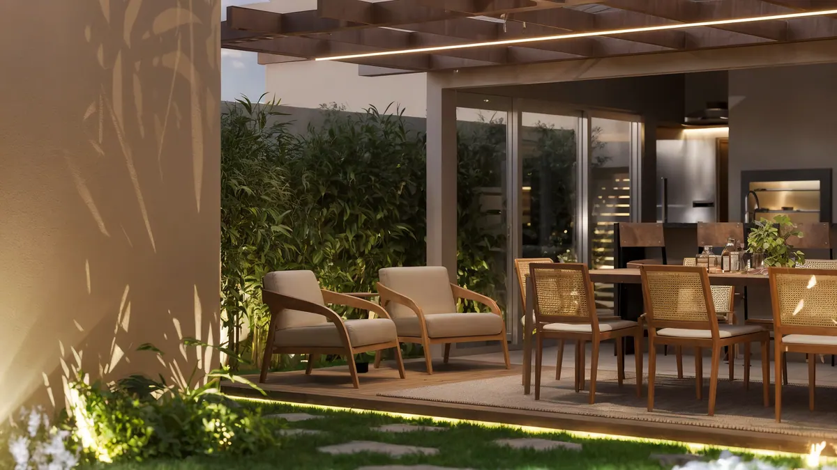 Poltronas e mesa de jantar sob o pergolado, com bambus e o jardim iluminado